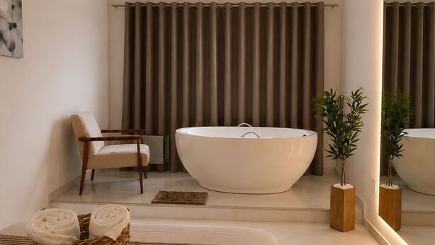 Une salle de bain moderne avec une grande baignoire, une chaise, un panier en osier rempli de serviettes et un miroir qui reflète la pièce.