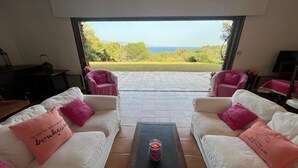 Ein Wohnzimmer mit weißen Sofas, rosa Kissen und Blick aufs Meer.