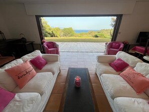 Ein Wohnzimmer mit weißen Sofas, rosa Kissen und Blick aufs Meer.