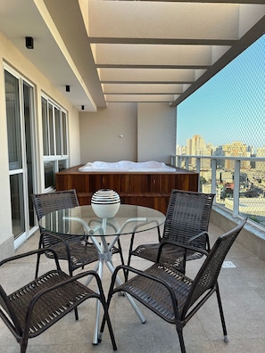 Ein Balkon mit Glastisch, Korbstühlen, einer Whirlwanne und Blick auf die Stadt.