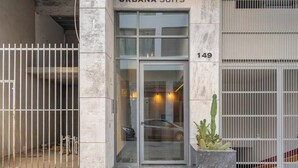 Entrada d'un edifici amb una porta de vidre, un cotxe visible a l'interior i una planta en test amb fora.