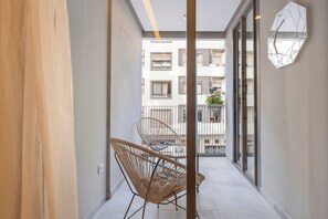 Ein schmaler Balkon mit Korbstuhl, einer Topfpflanze und einer geometrischen Wanddekoration.