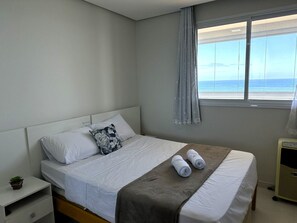 Une chambre d’hôtel avec un lit, une table de chevet, une fenêtre donnant sur la mer et un thermostat fixé au mur.