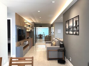 A modern living room with a sofa, a TV, and a dining area in the background. - Comfort & Design on Itaparica Beach (Vila Velha)