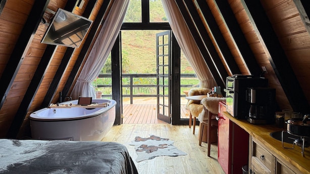 A cozy attic bedroom with a large window, a bathtub, a wooden desk, and a dog.