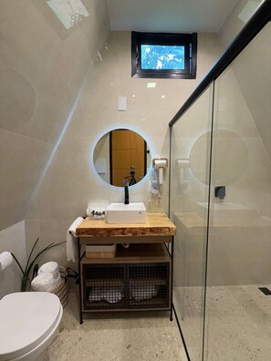 Une salle de bain avec un miroir rond, un meuble-lavabo en bois, des toilettes et un espace douche.