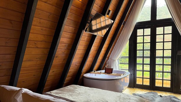 A bedroom with a sloped ceiling, a bed, a small table, and a window with curtains. - Cozy Chalet with Jacuzzi in Domingos Martins (Domingos Martins)