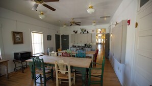 Un comedor con una mesa y sillas de madera, un ventilador de techo y una cocina al fondo.