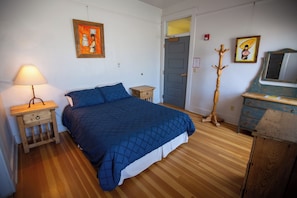A bedroom with a bed, a nightstand, a lamp, a dresser, a mirror, and two paintings on the wall.