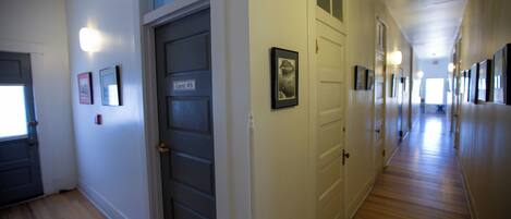 A hallway with a wooden floor, white walls, and doors marked with room numbers.