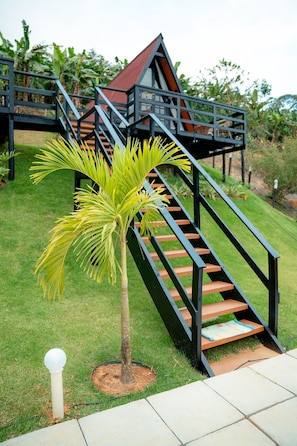 Eine Treppe führt zu einem Gebäude mit rotem Dach, umgeben von Grün und einer Palme.