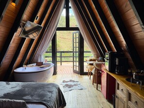 Un dormitorio acogedor en el ático con un ventanal grande, una bañera, un escritorio de madera y un perro.