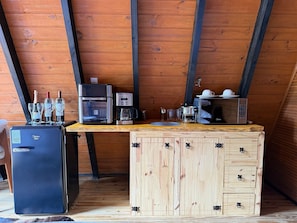 Eine kleine Küche mit Kühlschrank, Kaffeemaschine, Mikrowelle und Weingläsern auf einer Holz Arbeitsplatte.