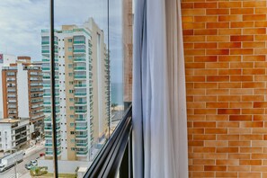 Blick aus einem Fenster mit Ziegelwand und Vorhang auf einen Stadtblick mit hohen Gebäuden und einer Straße.