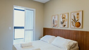 Una camera d'albergo con un letto, una testiera in legno, una finestra con tende e tre opere d'arte appese al muro.