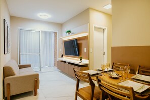 Ein modernes Wohnzimmer mit einer Couch, einem Esstisch mit Gläsern und einem Fernseher auf einem Schrank.