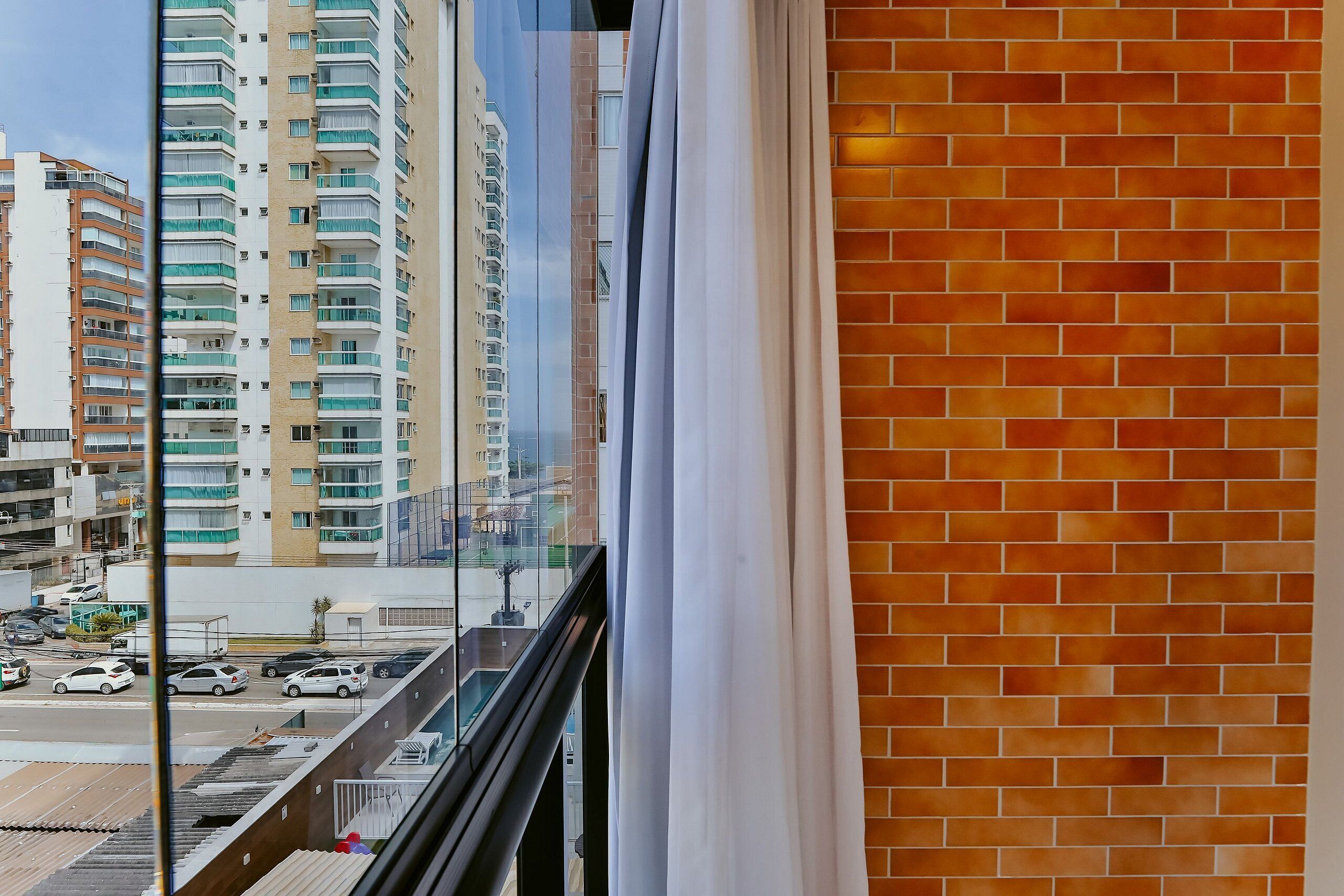 Une vue depuis une fenêtre donnant sur une rue, avec des voitures et des immeubles, dont un grand immeuble résidentiel doté de balcons.