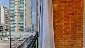 Vista dalla finestra su una strada con auto e palazzi, tra cui un alto condominio con balconi.