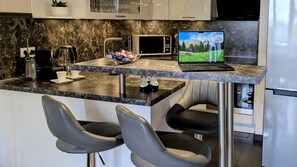 A modern kitchen with a marble countertop, a microwave, a laptop, and bar stools. - Vrbo Property (Schwarzenberg/Erzgebirge)