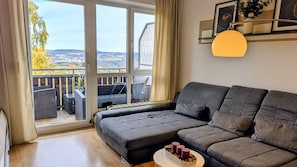 Ein modernes Wohnzimmer mit einem grauen Sofa, einem kleinen Tisch mit Kerzen und einem Balkon mit Korbmöbeln.