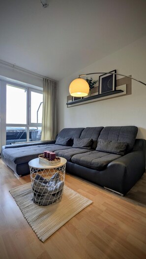 A modern living room with a sofa, a round table, a floor lamp, and a large window. - Vrbo Property (Schwarzenberg/Erzgebirge)