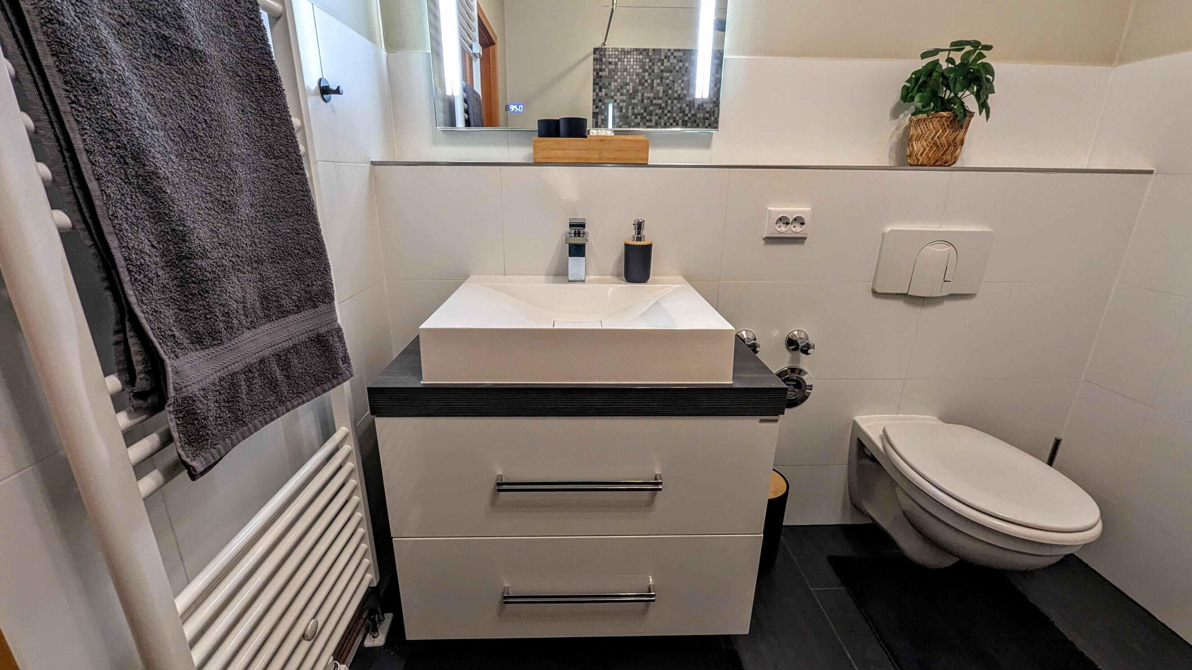 Un baño moderno con un lavamanos blanco, encimera negra y un inodoro.
