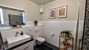 A modern bathroom with a white sink, toilet, and a mirror above the sink. There are two framed pictures on the wall and a potted plant on a wooden shelf. - Vrbo Property (Schwarzenberg/Erzgebirge)