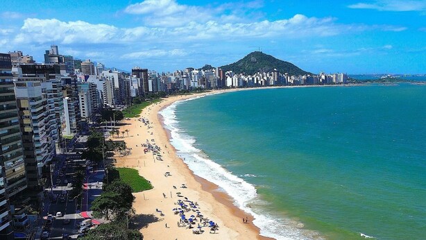 Paisagem costeira com uma montanha imponente, edifícios altos e uma praia.