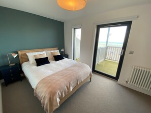 Une chambre à coucher comprenant un lit, des tables de chevet, une lampe, une fenêtre et une porte donnant sur un balcon.