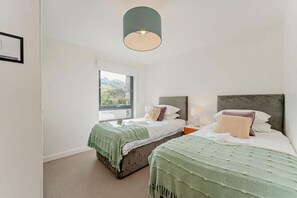 Une chambre avec deux lits, une grande fenêtre et un luminaire suspendu.
