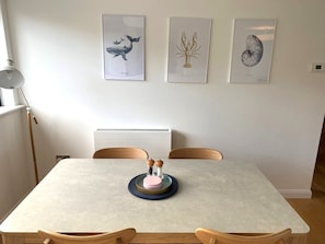 Ruokailutila, jossa on pöytä, tuoleja, seinälle ripustettuja taideteoksia ja lamppu.
