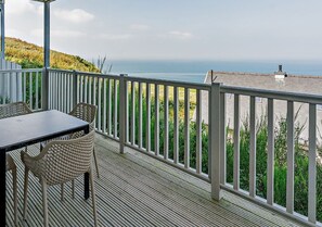 Un balcon avec vue sur la mer, une table et deux chaises en osier.