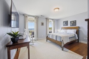 Ein Schlafzimmer mit einem Bett, einem Schreibtisch mit Pflanze, einem Sessel und einem Fenster mit Vorhängen.