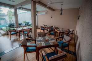 A restaurant with multiple tables and chairs, large windows, and ceiling fans. - Sea La Vie Hotel Negombo (Negombo)