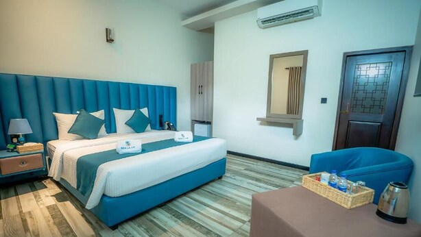 A hotel room with a bed, a nightstand, a chair, a small table with a basket and a kettle, and a wardrobe.
