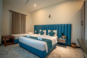 Een tweepersoonsbed met een blauw hoofdeinde, een nachtkastje met een lamp en een klein houten krukje.