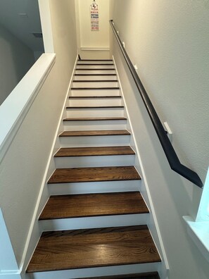 Eine Treppe mit Holzstufen und weißen Wänden, die zu einem Zwischenpodest mit einem Schild führt.