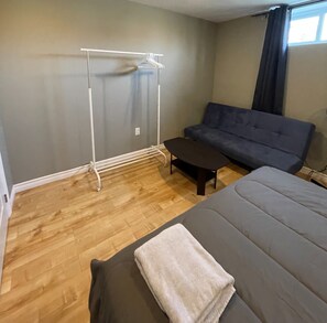 Ett rum med en säng, en soffa, ett litet bord, ett torkställ och ett fönster med gardiner.