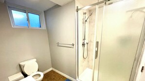 A bathroom with a toilet, a shower enclosure, and a window. - Basement Queen Bedroom-E（Private Room，Shared Bathroom） (Greater Sudbury)