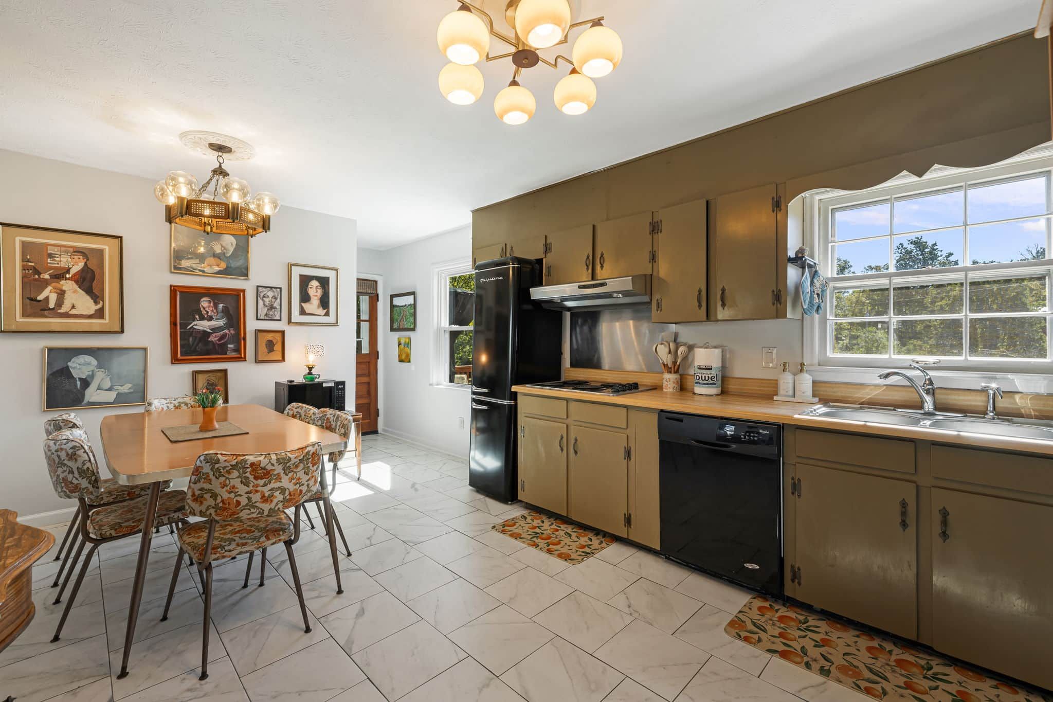 A kitchen with a dining area, featuring a chandelier, framed artwork, and a window with a view.