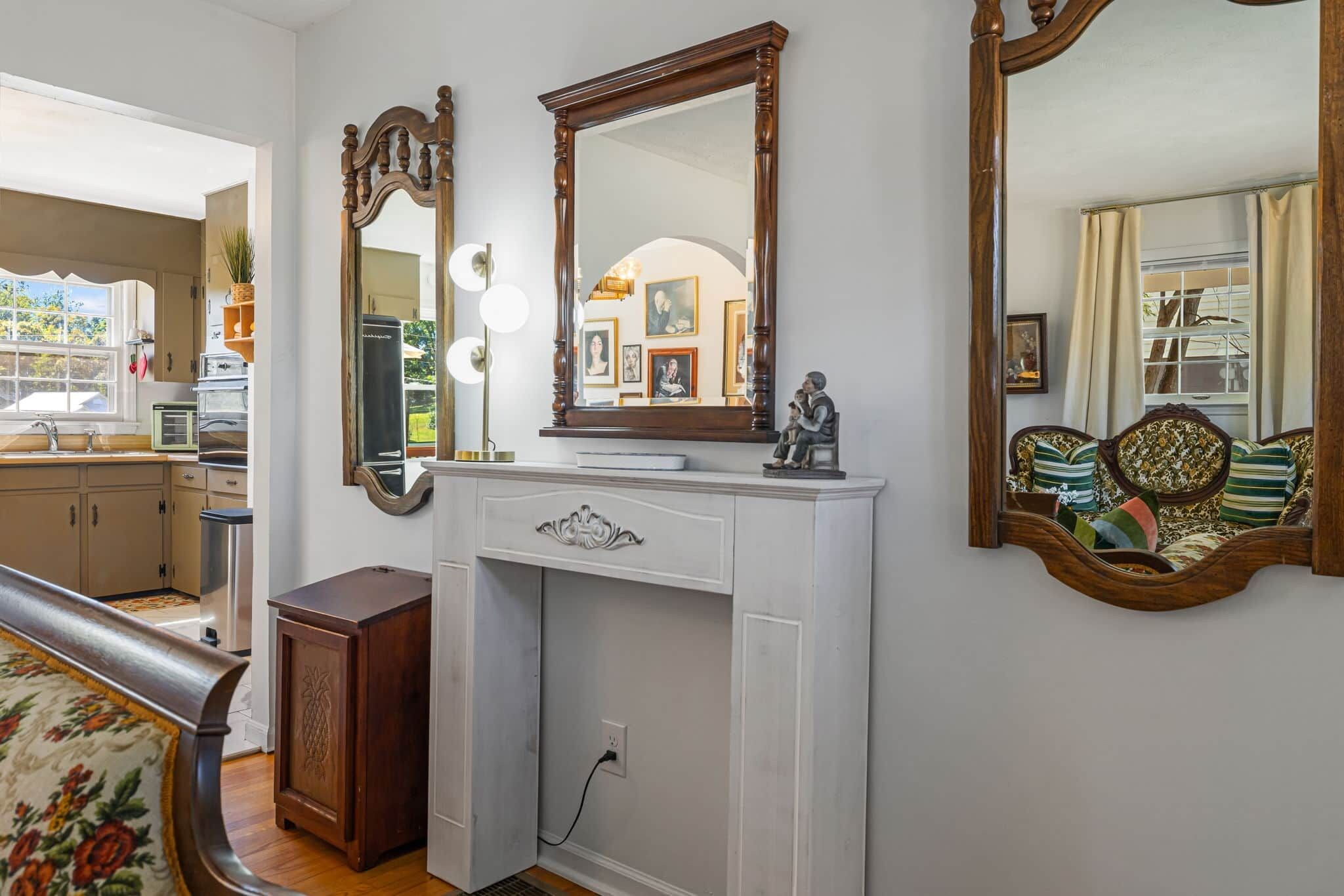 A room with a white dresser, a large mirror, and a sofa with patterned cushions.