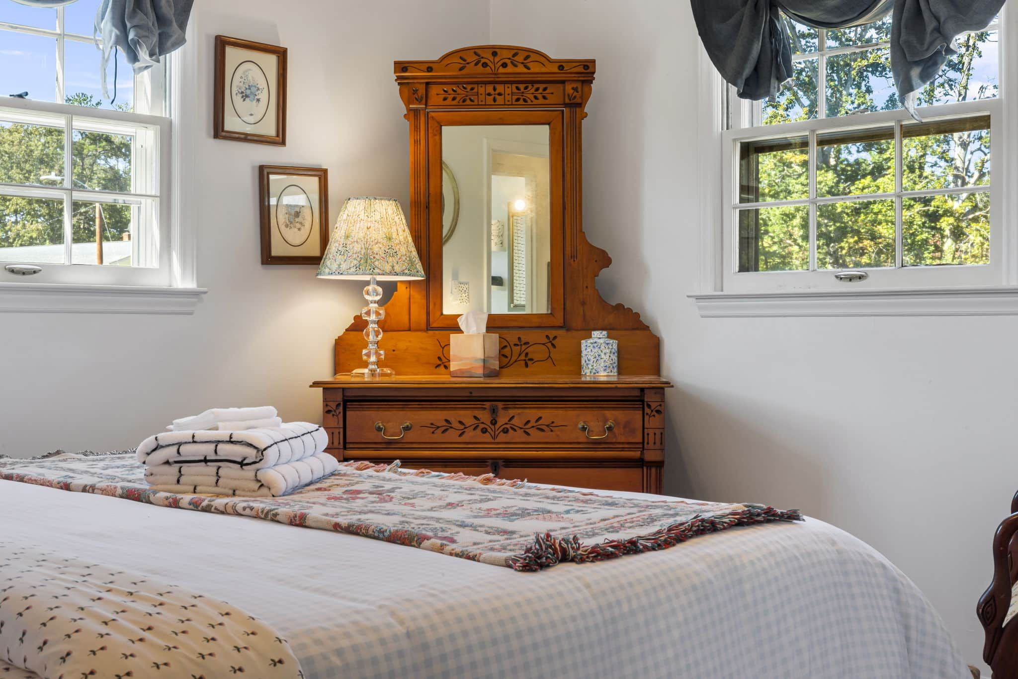 A bedroom with a bed, a dresser with a mirror, a lamp, and a window with curtains.