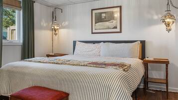 Ein ordentlich bezogenes Bett mit einer gestreiften Tagesdecke, ein Kopfkissen mit Blumenmuster und ein Nachttisch mit einer Lampe.