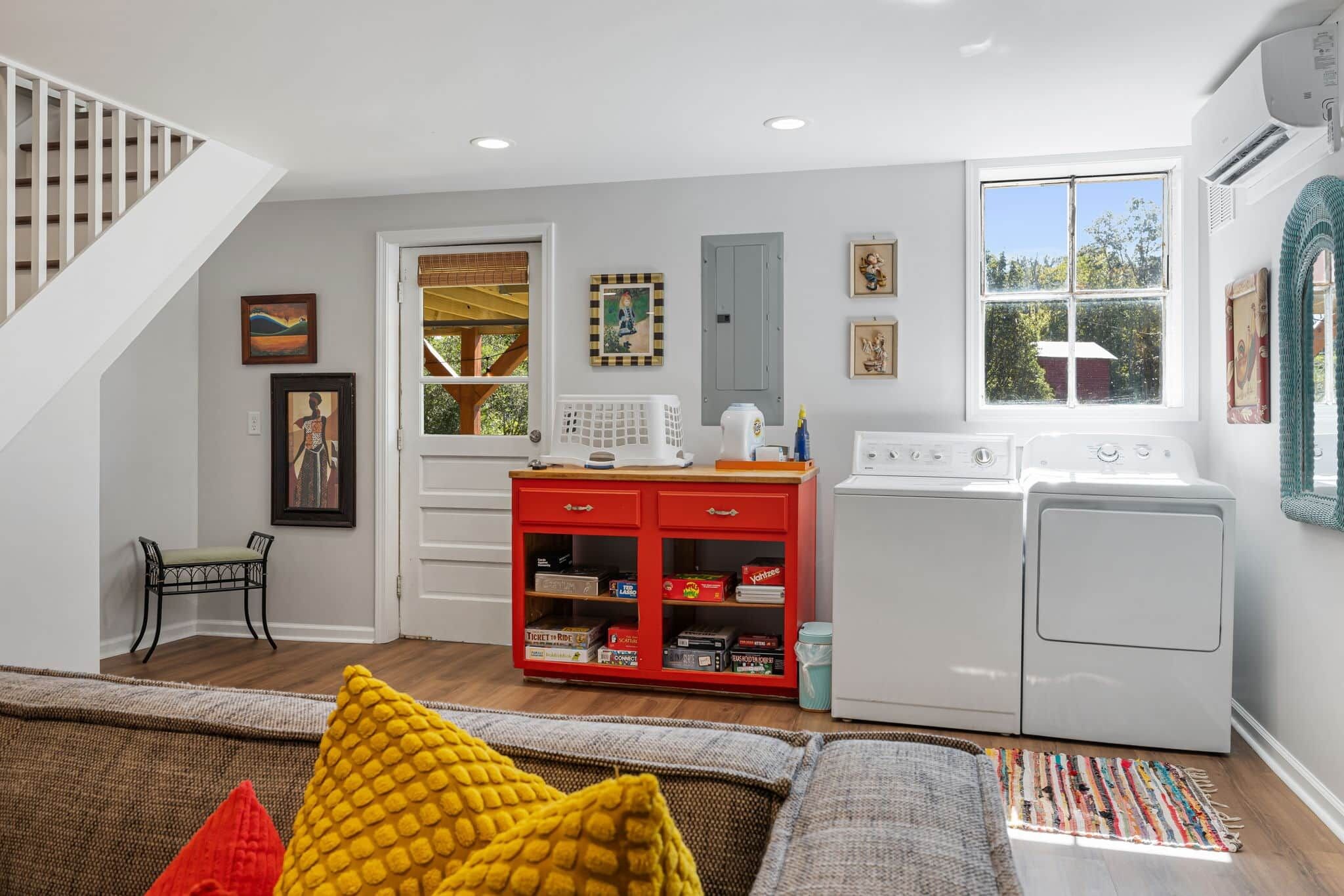 A compact living space with a staircase, a red entertainment unit, a washing machine, and a window with a view.