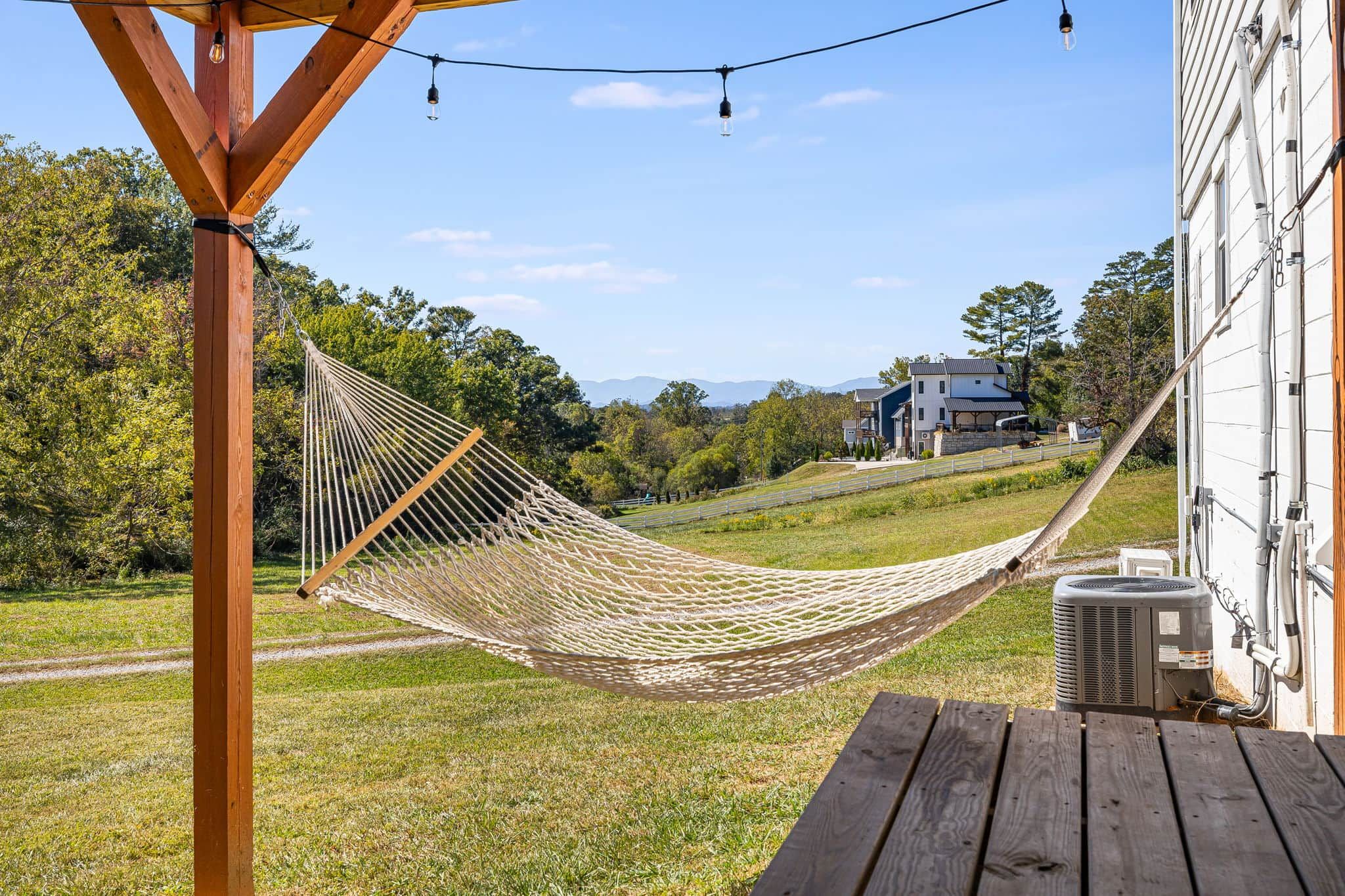 A hammock on a wooden deck with a view of a house and trees in the background.