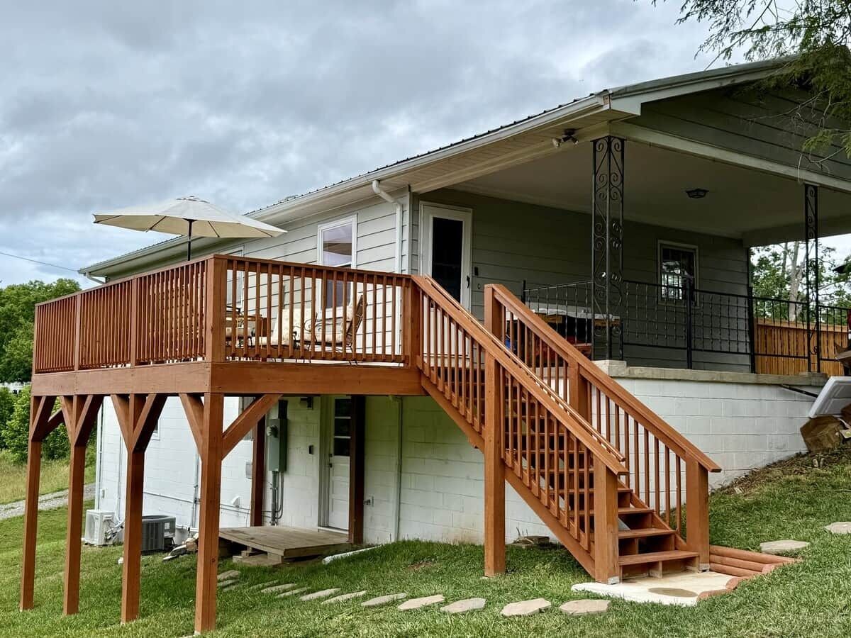 A two-story house with a wooden deck, a staircase, and a covered porch.