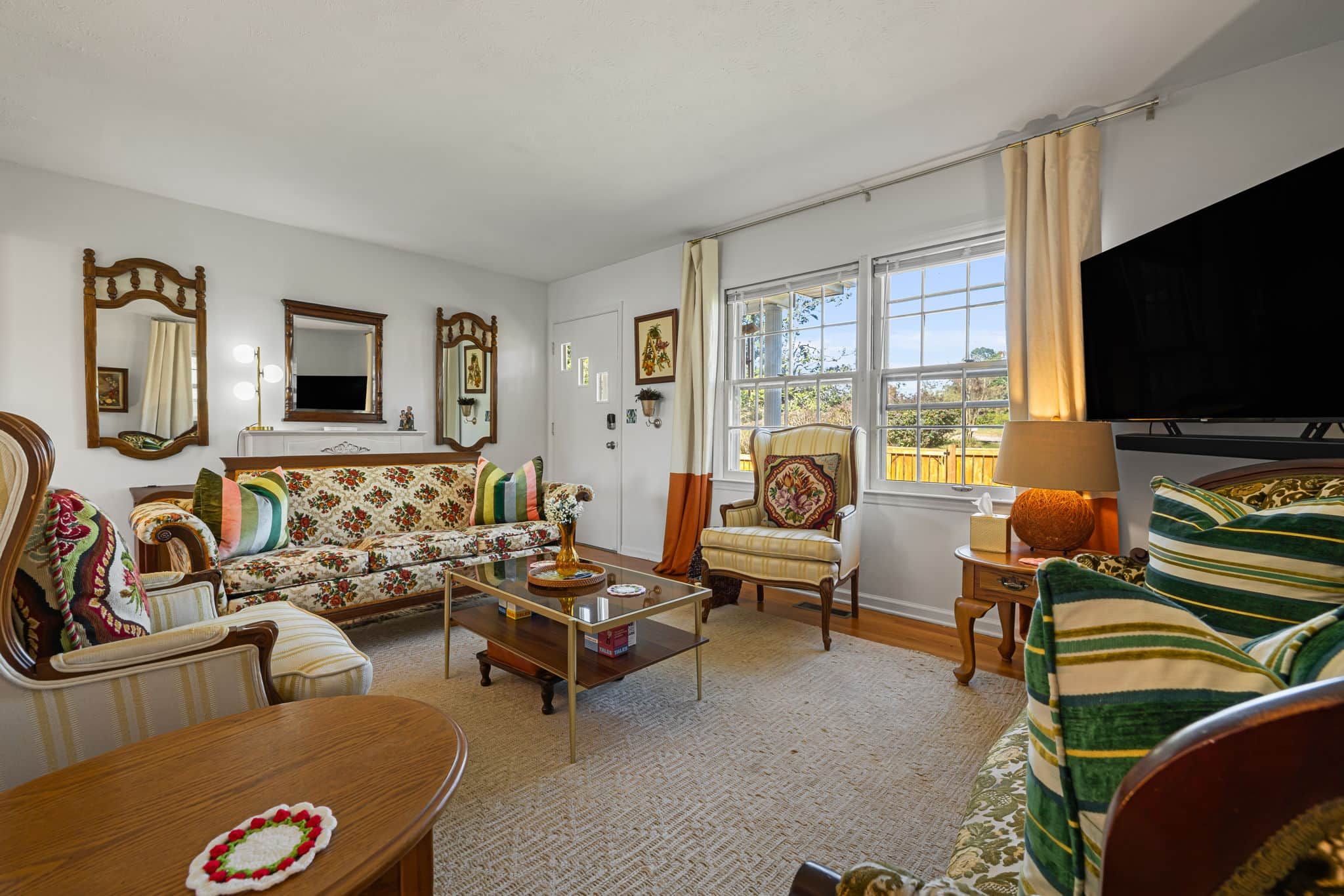 A living room with a sofa, armchairs, a coffee table, a television, and a large window with curtains.