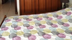 Un dormitorio con un armario de madera, una cama con colcha de lunares y una lámpara sobre la mesita de noche.