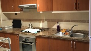 Una cocina con armarios de madera, un lavamanos de acero inoxidable y una encimera con un hervidor y una botella.