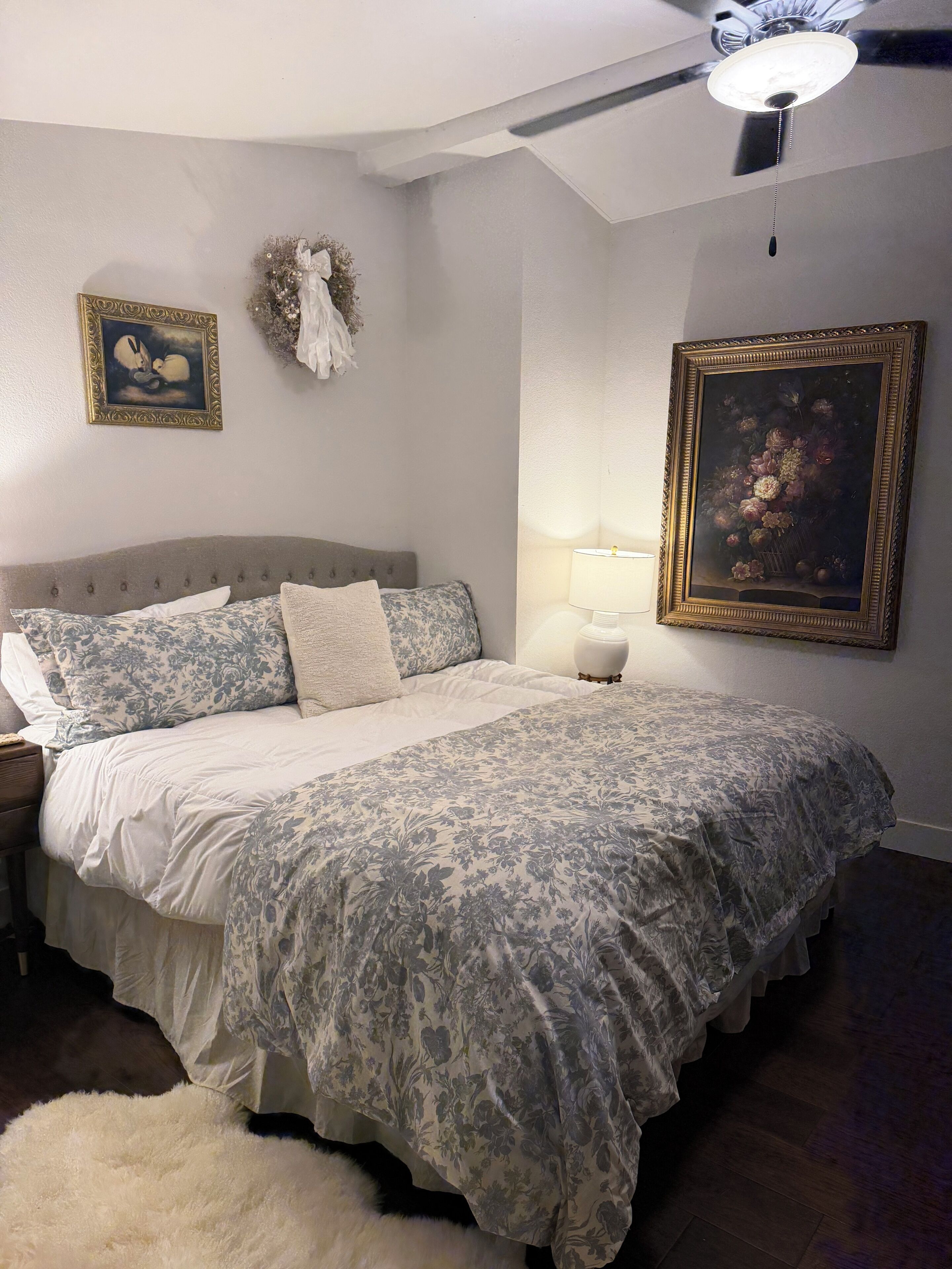 Une chambre à coucher avec un lit, une table de chevet, des œuvres d’art murales et un ventilateur de plafond.